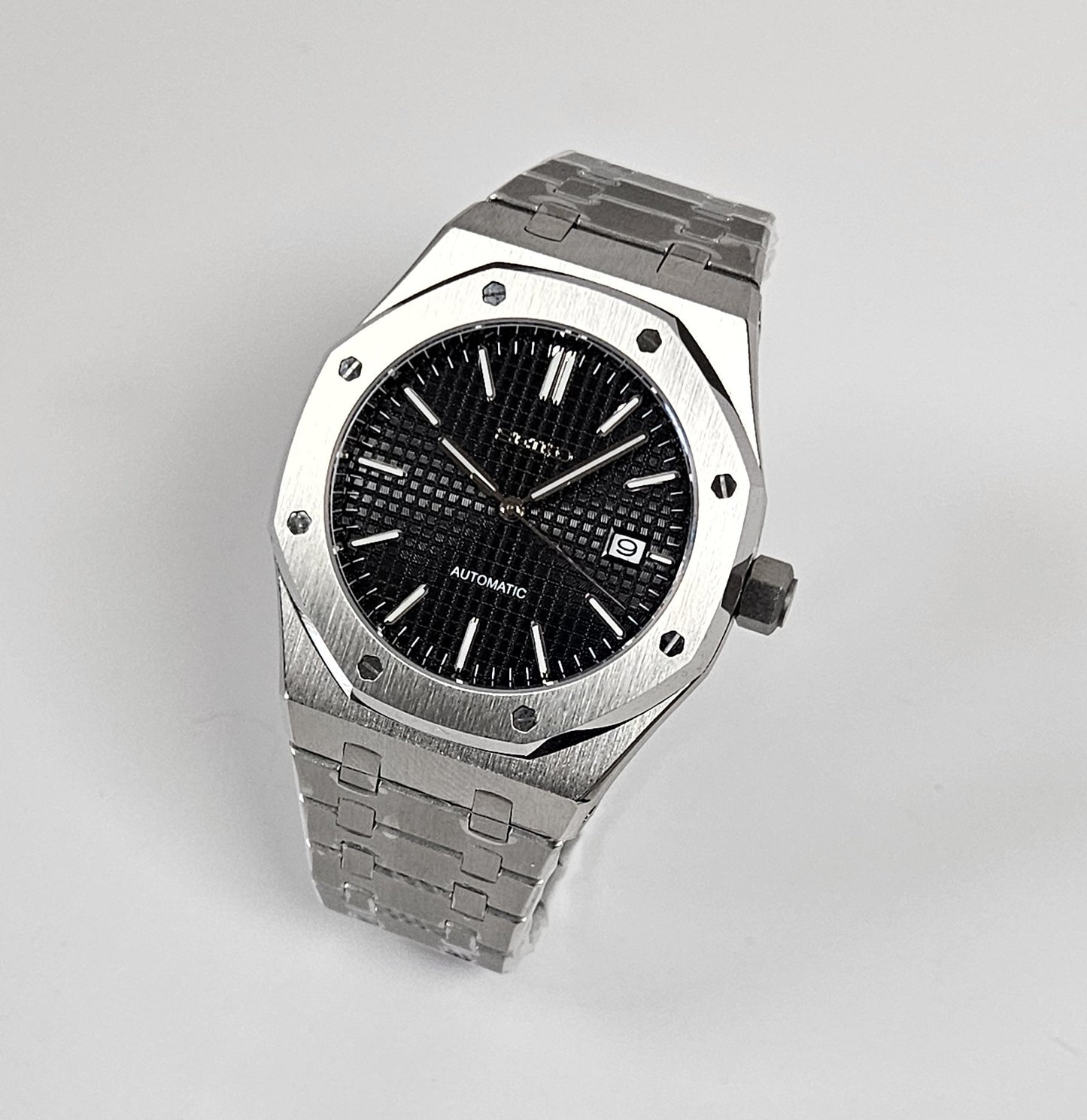 A black dial Royal Oak Seiko Mod watch with a stainless steel bracelet and a screw down case back.