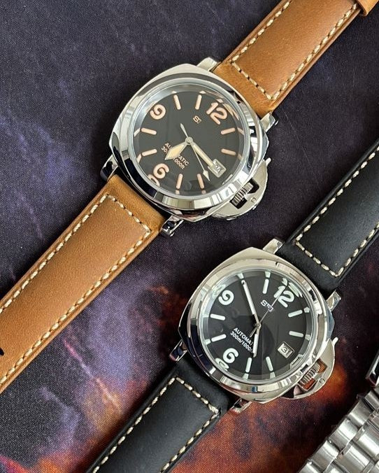 Two watches with brown and black leather straps on a textured surface