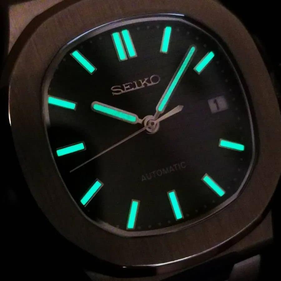 Seiko watch with glowing green hands and markers on a dark background