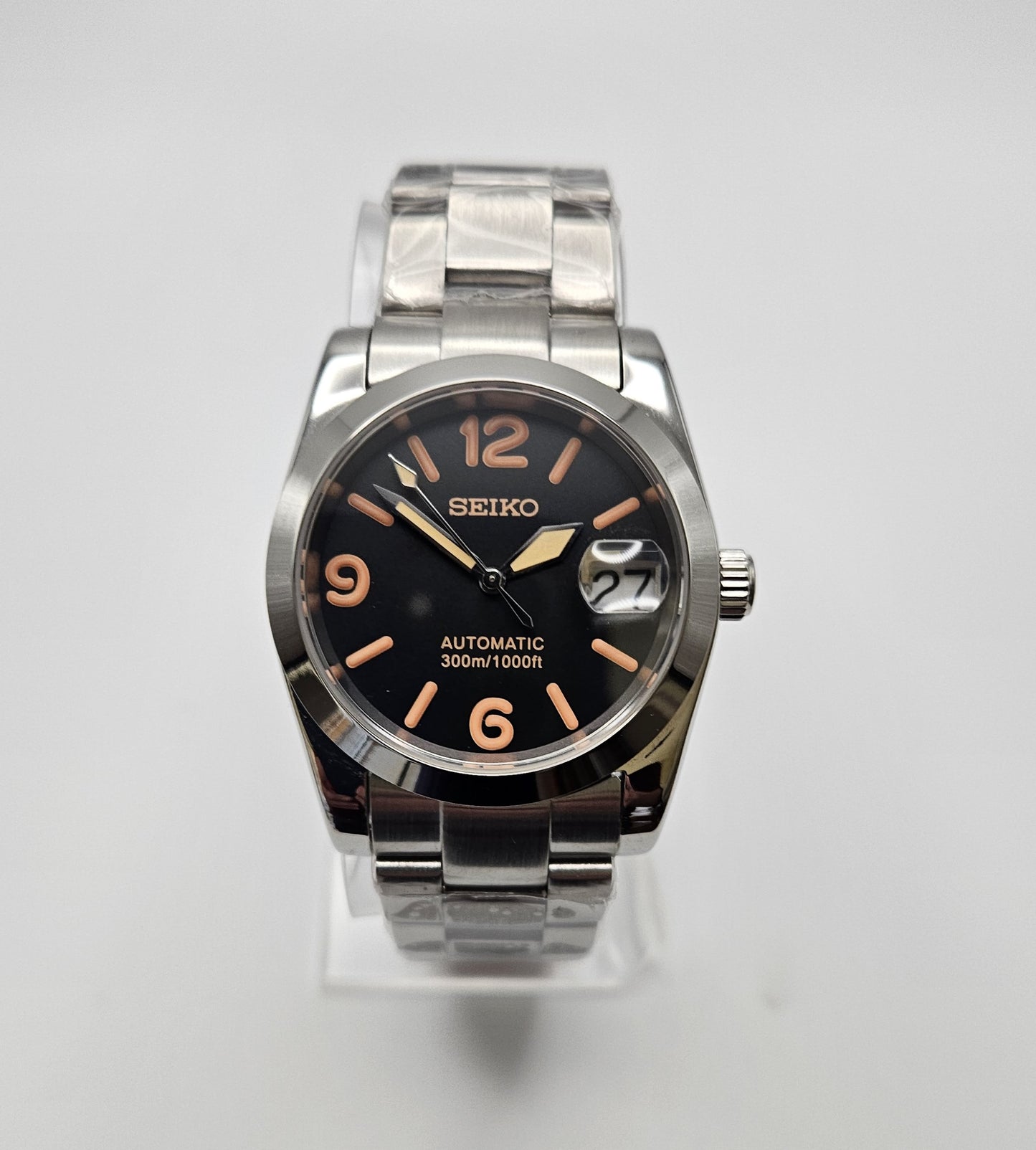 Seiko watch with black dial and silver metal band on a white background
