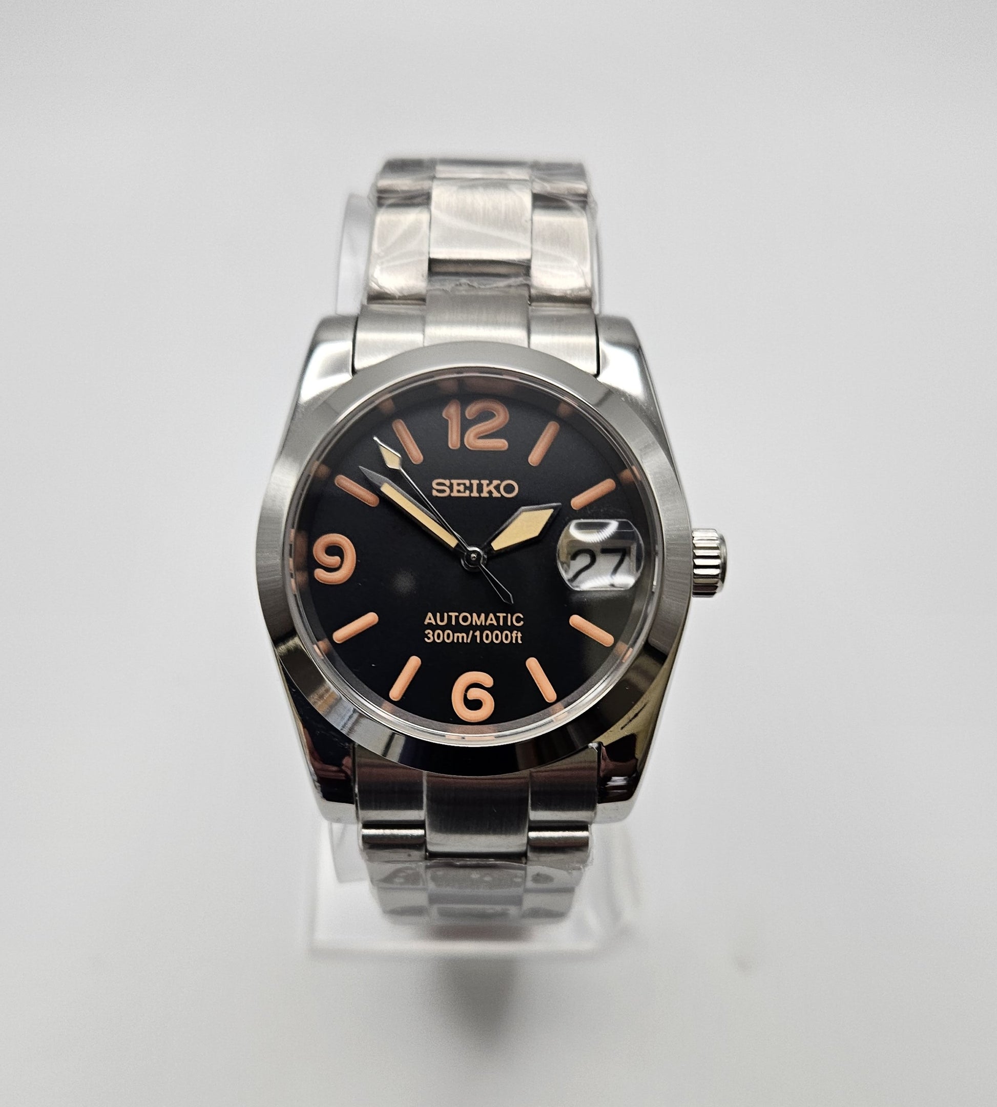 Seiko watch with black dial and silver metal band on a white background