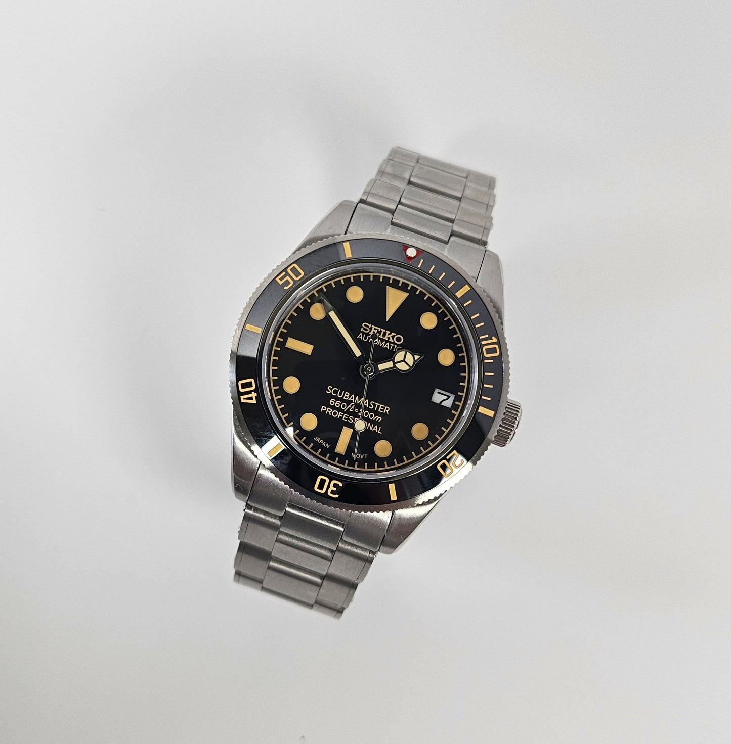 Seiko watch with black dial and silver metal strap on a light gray background