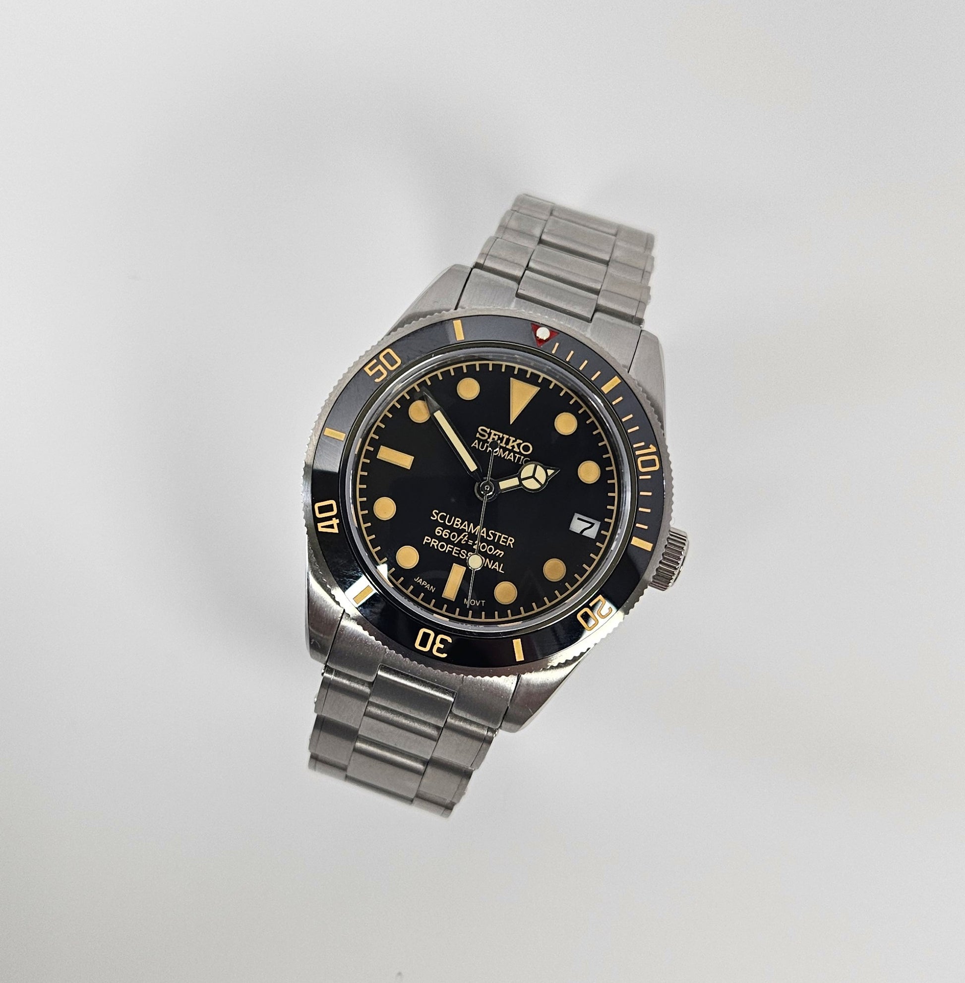 Seiko watch with black dial and silver metal strap on a light gray background